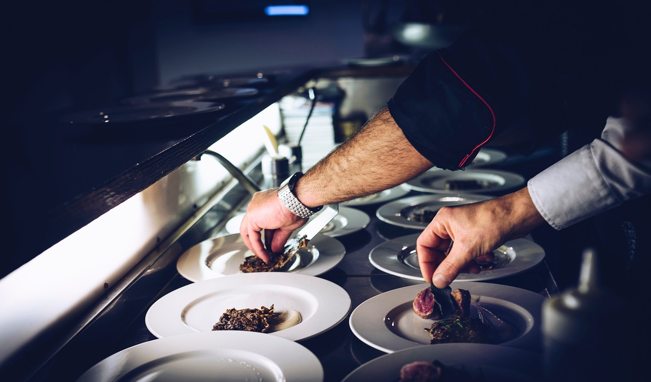 Professional catering team collaborating in an open kitchen, plating dishes with precision under warm overhead lighting.
